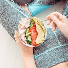 Una persona con ropa deportiva comiendo un bol de ensalada con pollo, tomate y aguacate